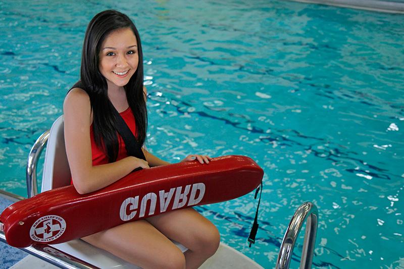 Lifeguard sits in front of a pool wearing a red suit